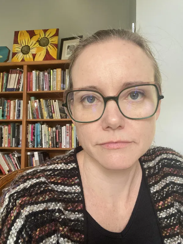 woman in glasses and a striped sweater in front of a bookcase